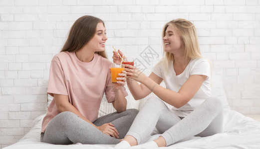 两个女朋友在床上聊天微笑和喝新鲜的冰沙子图片
