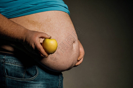 胖子在裸露的胃前拿着苹果饮食和健康饮食的概念图片