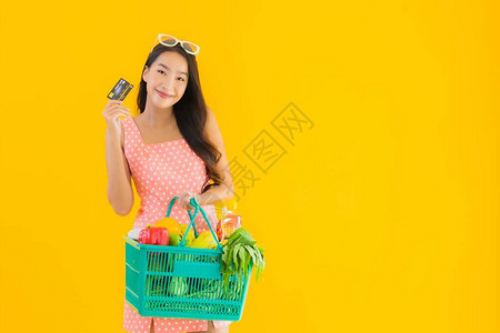 超市果蔬在超市的篮子购物和黄色孤立背景的信用卡上提供杂货的美丽年轻的年轻亚洲妇女背景
