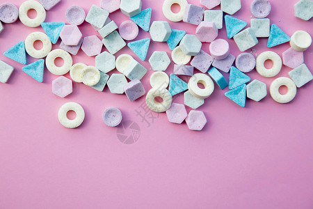 粉红色背景上隔开的多彩糖果自然光图片