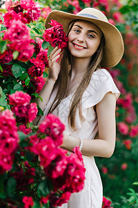 穿着夏裙的年轻美女在公园里露着玫瑰花的灌木丛旁戴着女装和女人图片