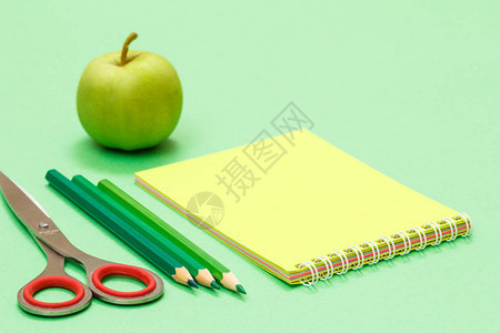 剪刀彩色铅笔记本和绿色背景上的苹果回到学校的概念学校图片