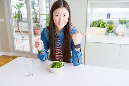 美丽的亚洲女人吃青绿新鲜西兰花指向并用大拇指露面笑图片