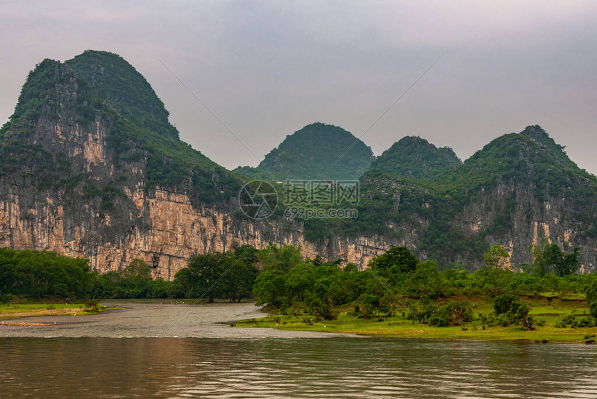 沿漓江景观与绿色森林喀斯特山脉与深灰色天空下的棕黑色垂直悬崖一些树木图片