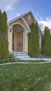 垂直庭院和锥形树在蓝天和云彩下的家门面狭窄的通道和楼梯通向拱图片