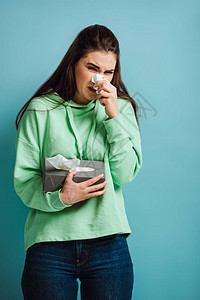 生病的女孩用蓝色背景的纸巾擦鼻子图片