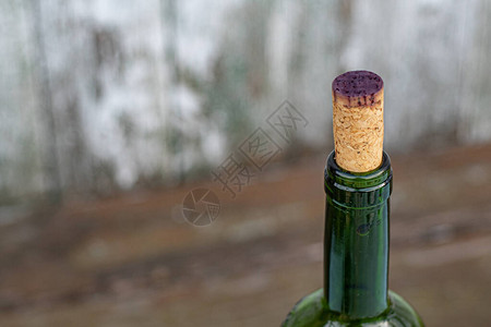 红酒背景葡萄酒瓶颈的特写镜头用被深紫色红酒染色的软木塞封闭仿旧木背景上的绿色玻璃瓶顶部背景