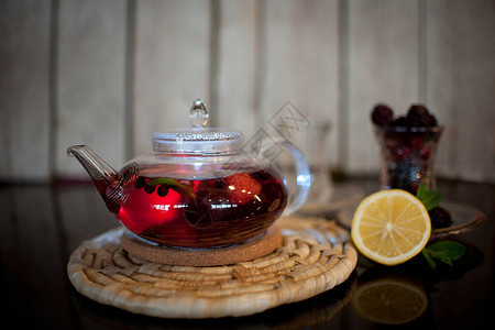 红茶和浆果在透明的圆茶壶中在木架上图片