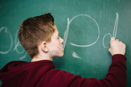 高等学校的学生穿着深色连帽衫站在教室写字母表的绿色黑板附近图片