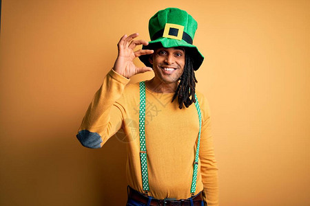 戴绿色帽子庆祝圣徒节的年轻非洲男子微笑并自信地驾驭手势图片