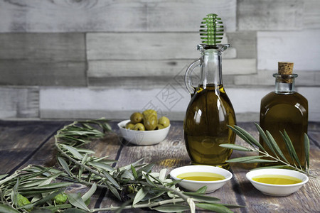 两个油瓶碗里的一把绿橄榄橄榄枝和木桌和木背景图片