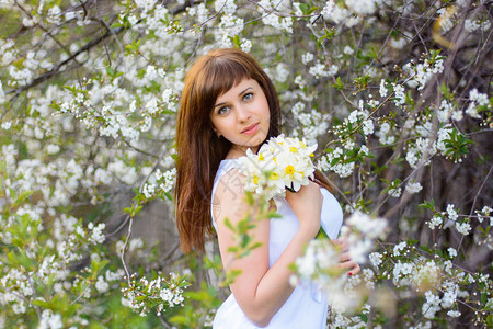 美丽的年轻女孩带着一束花水仙子穿着白色洋装在春天樱图片