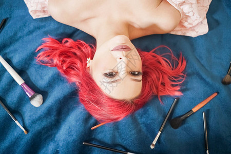 穿着红发的漂亮女人躺着化妆刷子和做梦顶尖风景女孩在蓝图片