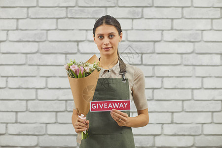年轻女花店的腰部肖像举着GIVEAWAY标志图片