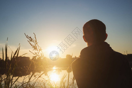 日落时一个年轻人坐在湖边的草地图片