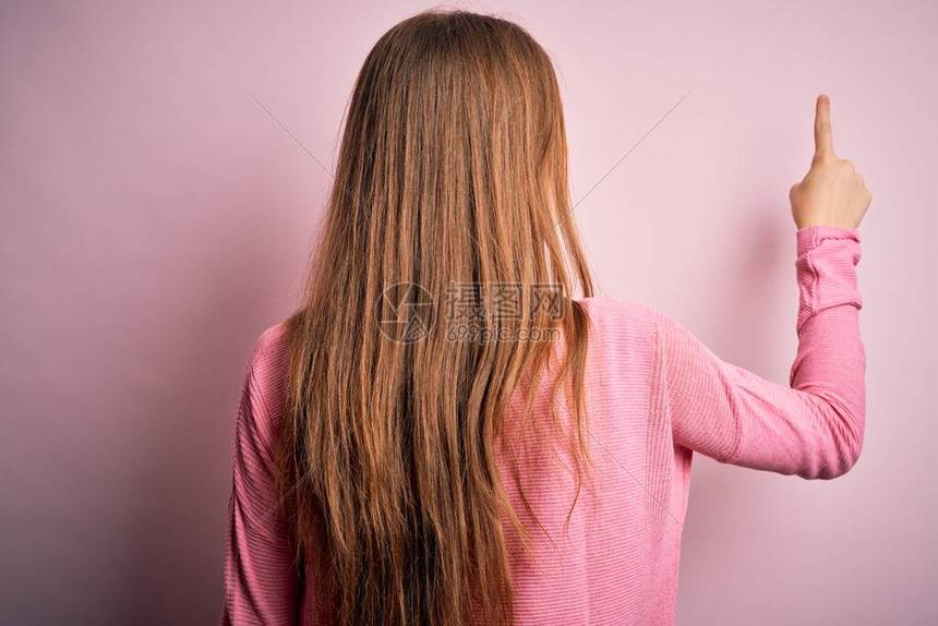 年轻漂亮的红发美女穿着随身毛衣穿着孤立的粉红色背景背向后图片