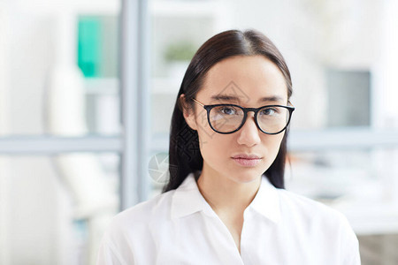 身戴眼镜看着相机的亚洲年轻女商人头部和肩膀肖像图片