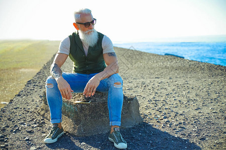 沉思的老人坐在户外思考一个人站在破旧的码头上凝视着大海一位长着灰胡子戴着眼镜坐在石头上的忧心忡的老人图片