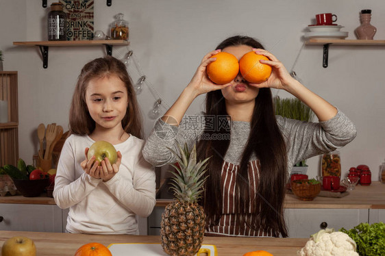 有趣的母亲和她的女儿正在切水果和愚弄图片