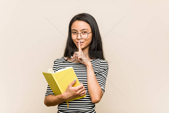 年轻亚洲女学生持有一本书保守秘密或要求保持沉默图片
