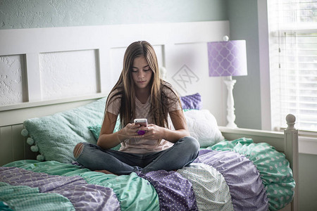 青少年女孩用智能手机发短信坐在她卧室的图片