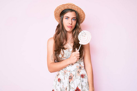 戴着夏帽和棒糖的美丽年轻白人女思维态度和清醒的表情图片