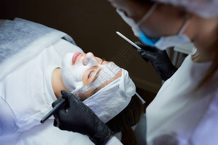 她在女孩的脸上涂去皮的gommage在美容院进行皮肤清洁手术时图片