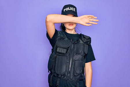 身穿紫色背景安全防弹背心制服的年轻女警用手臂遮住眼睛图片