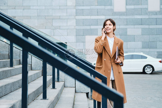 带着笔记本电脑的年轻笑着的临时女商务女青年穿着大衣图片