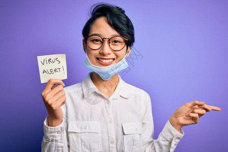 戴着医用口罩的年轻漂亮亚洲女孩拿着带有警报信息的提醒图片