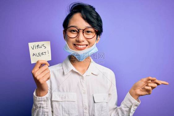 戴着医用口罩的年轻漂亮亚洲女孩拿着带有警报信息的提醒图片