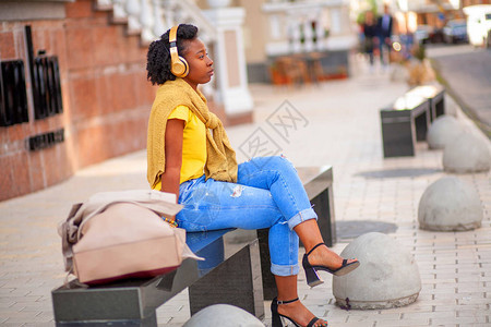 生活方式街头女孩身穿黄色T恤和蓝色牛仔裤的非裔美国女孩站在城市街道上时尚的女人漂亮地摆姿势拍照她非图片