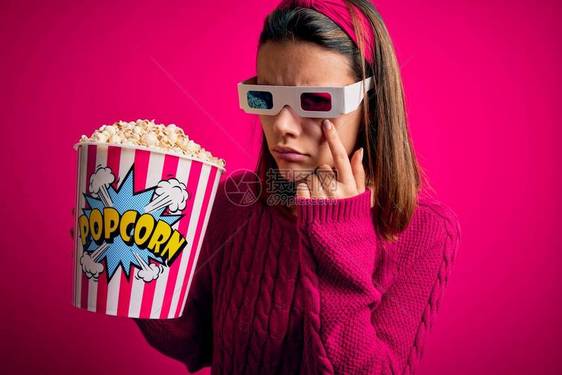 年轻漂亮的女孩用3d眼镜吃爆米花的盒子看电影指着眼睛看着你的手势图片