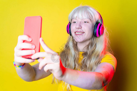 年轻美丽的白种女人在粉红色背景下自拍孤立的金发年轻女子戴着耳机工作室拍摄直播社交网络技术背景图片