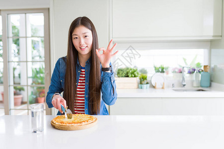 美丽的亚洲女人吃和切象棋比萨做好用手指的标志图片