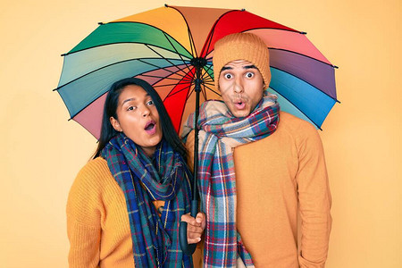 彩色雨伞下美丽的拉丁年轻夫妇惊恐地张大嘴巴图片