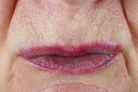一位老年妇女紧挤压的狭窄粉红色嘴唇在宏观照片中可以清楚地看到毛图片