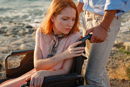 坐在轮椅上的红头发女人在日落时分在海边和她的伴侣聊天夏季图片