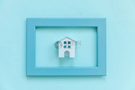 简单地设计与蓝色框架中的微型白色玩具屋隔离在蓝色柔和的彩色时尚背景上抵押财产保险梦想家园概念平躺顶图片