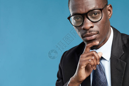 穿着西装和戴眼镜的非洲成衣商人肖像与眼镜中商人在蓝背景上思考图片