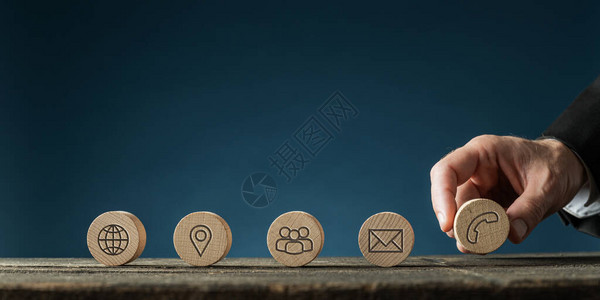 一个商人的手在质朴的木制桌子上连续放置五个带有联系人和信息图标的木制切割圆圈在与复制空图片