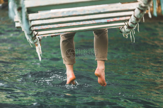 坐在悬浮桥上的男子将腿放入海水中图片