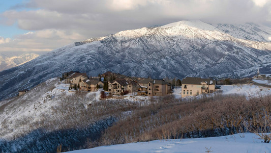 全景瓦萨奇山脉的原始景观及其积雪覆盖的地形上的房屋在多云的蓝天下图片