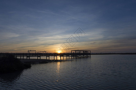 夕阳下平静的海水中倒映着木制码头的海岸景观图片