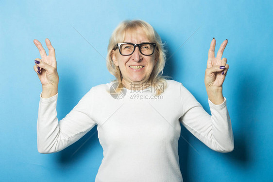 身戴眼镜面容快乐的老妇人用双手对蓝背景做出手势概念上幸福心情好一切都很好但图片