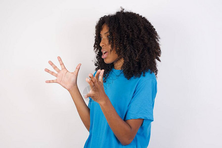 身着卷发的非洲青年妇女穿着轻便蓝衬衫站在白色背景面前大声喊叫图片