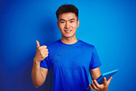 年轻的亚洲华人使用平板电脑站在孤立的蓝色背景上图片
