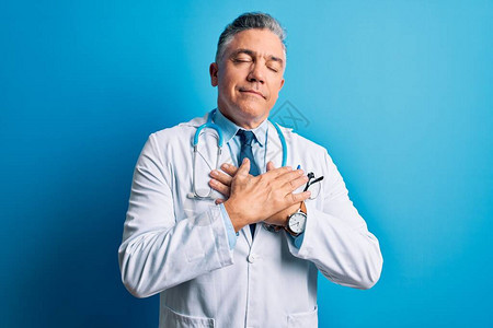 身着大衣和蓝色听诊器的中年长英俊的灰发医生男子在胸前微笑图片