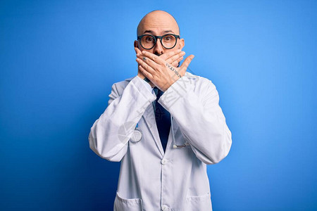 穿戴眼镜和听诊器的长胡子的光秃大脸的医生在蓝色背景下用双手遮住嘴顶图片