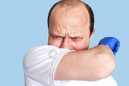 成年男子在肘部咳嗽被蓝色背景孤立科图片